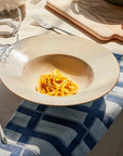 Off white speckled pasta plate with pasta inside on set table.