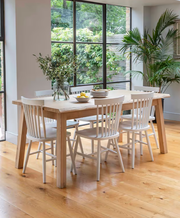 Oak dining table, set with tableware and surrounded by white farmhouse dining chairs.