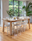 Oak dining table, set with tableware and surrounded by white farmhouse dining chairs.