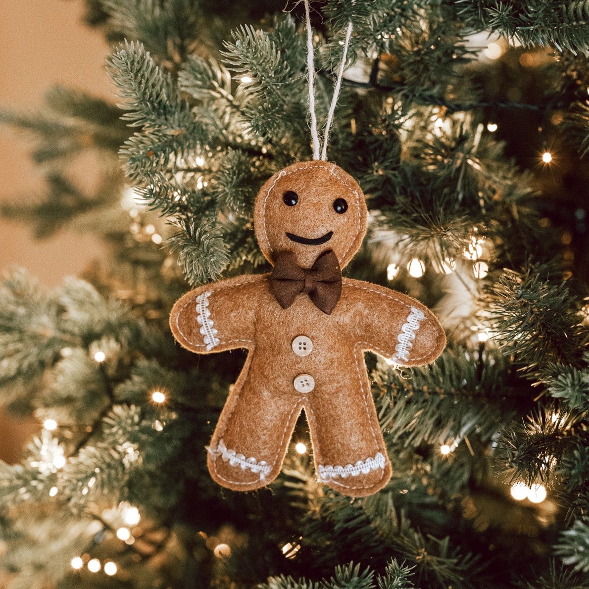 Brown hanging gingerbread Christmas decoration with bow tie and smiley face on green Christmas tree with lights.