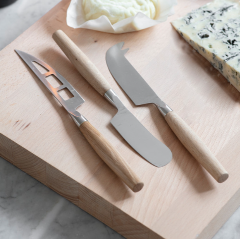 Cheese knife set of three on wooden chopping board with cheese.