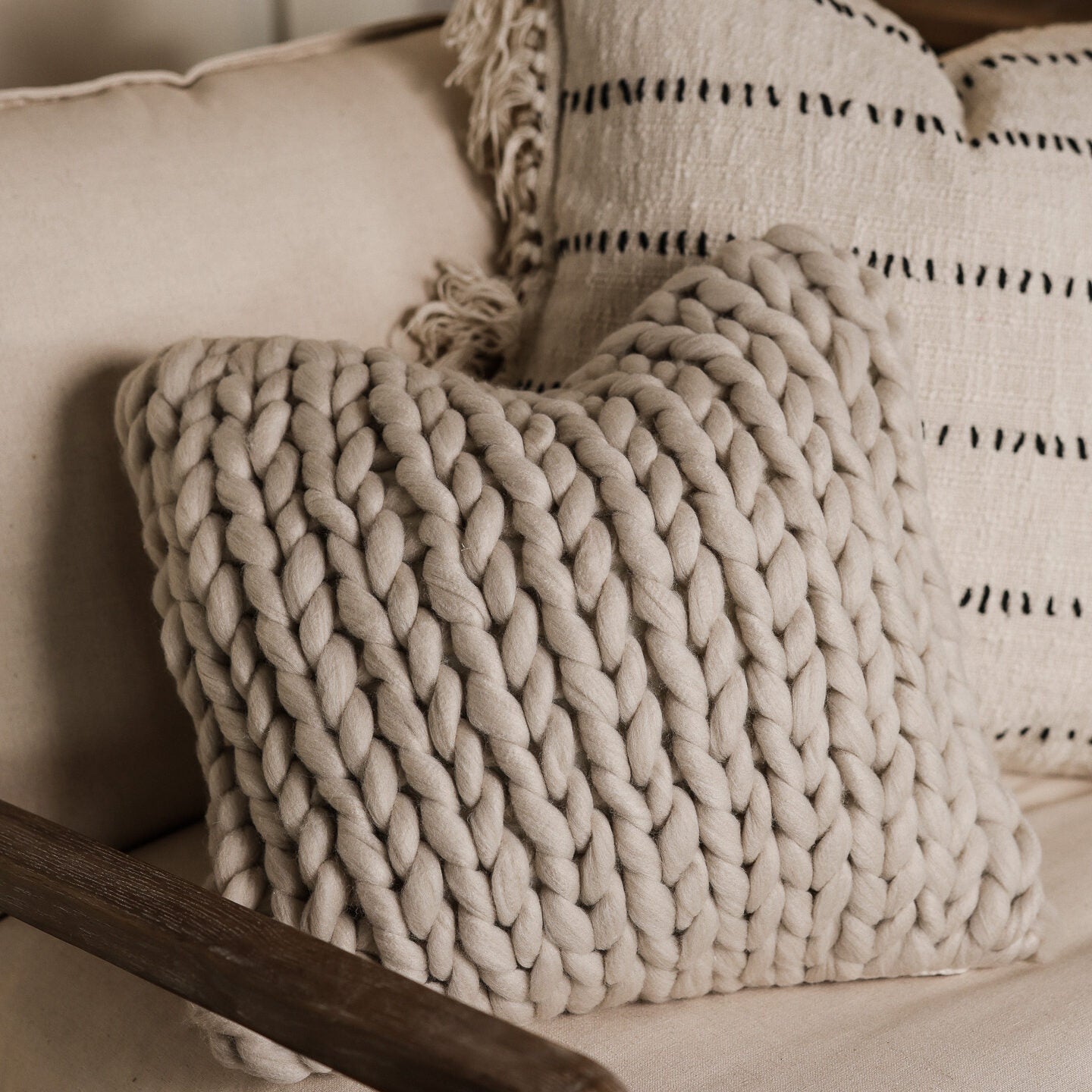 Beige knitted cushion cover on armchair with striped cushion behind.