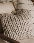 Beige knitted cushion cover on armchair with striped cushion behind.