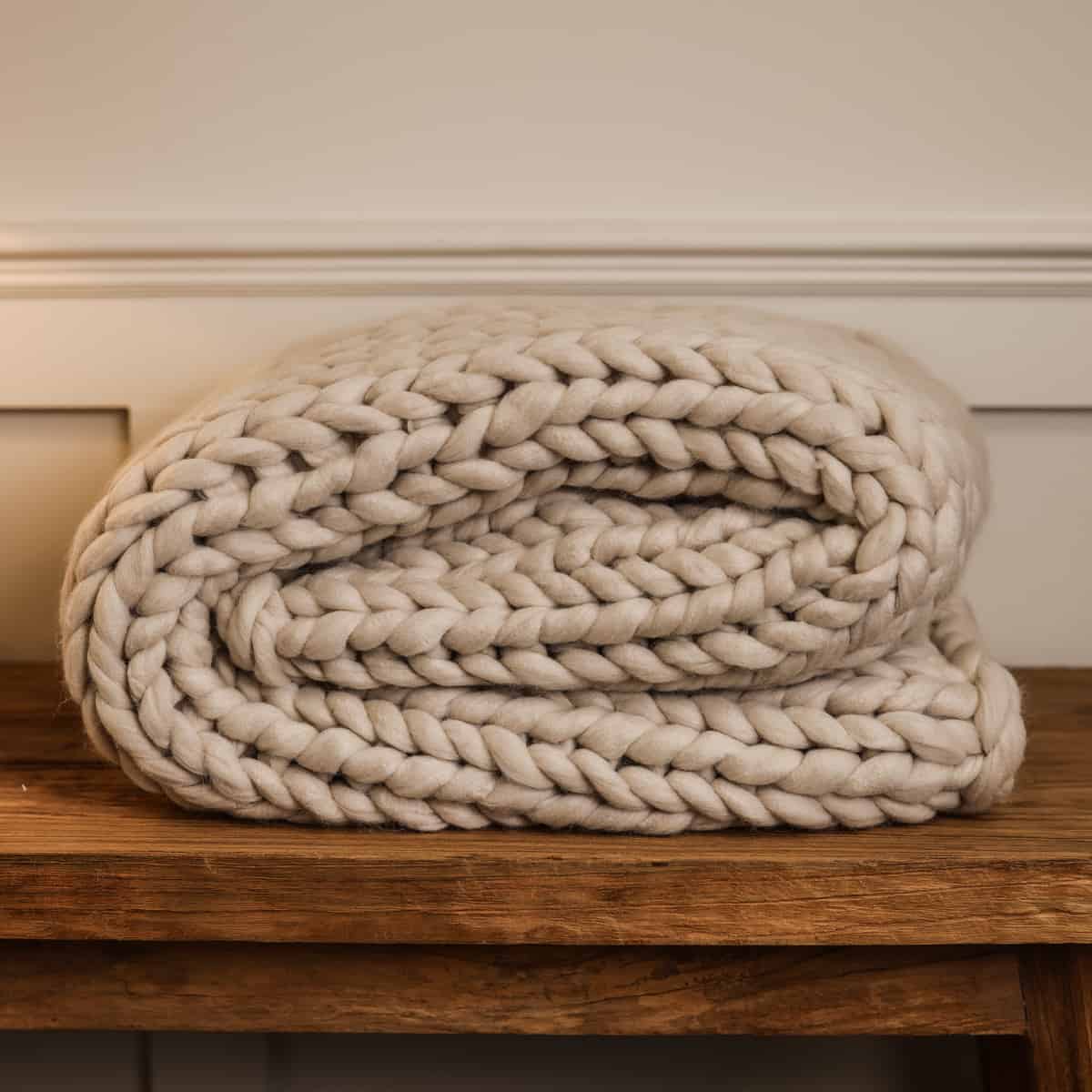 Chunky cream knitted blanket folded up on console.