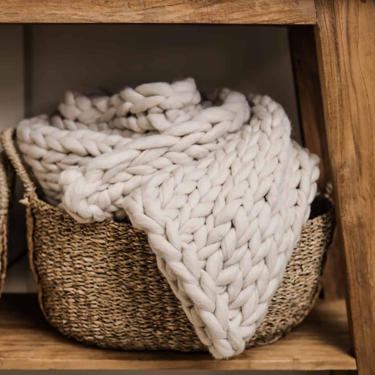 Chunky knitted blanket rolled up in a woven wicker basket.