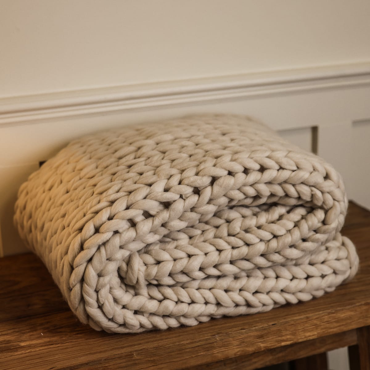 Chunky knit blanket folded up on a wooden console side view.