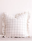 A white ruffle cushion featuring a slate grey grid stripe.