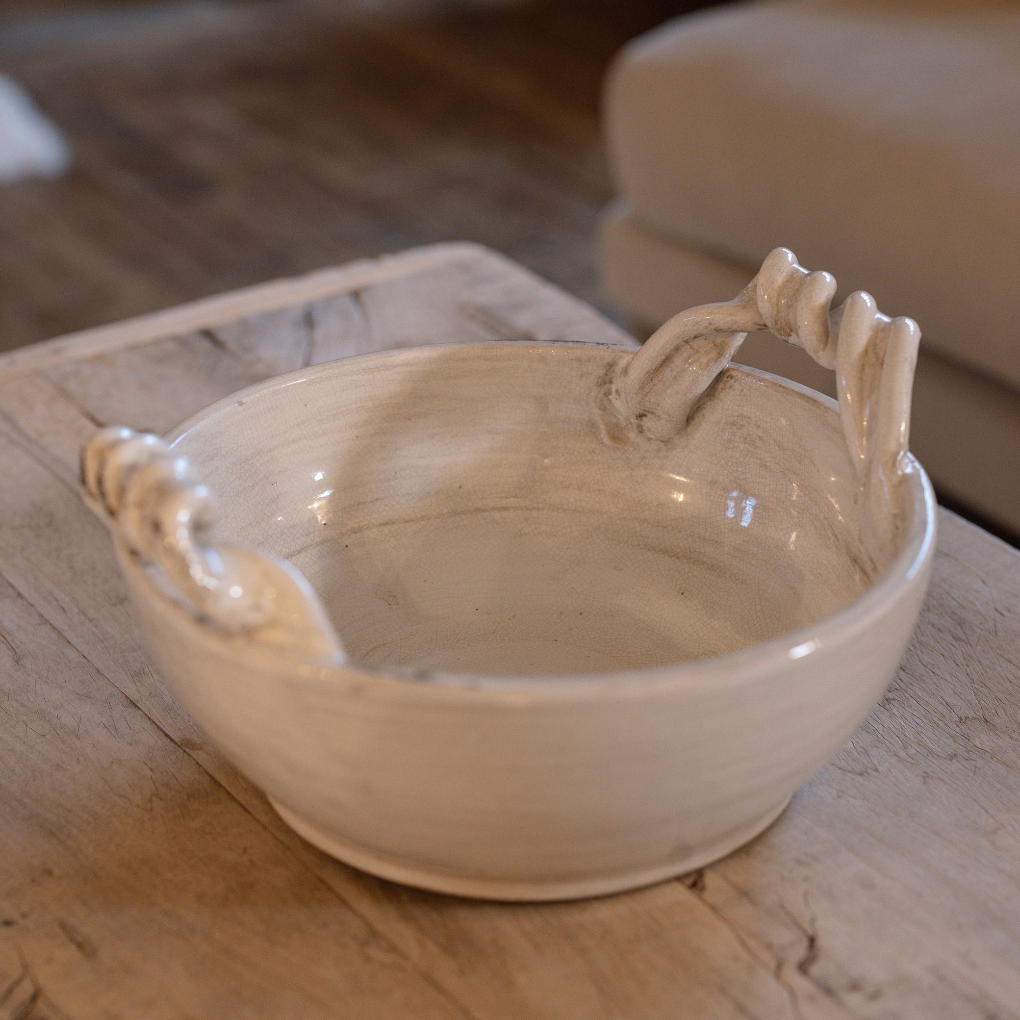 Off white ceramic bowl with twisted handles on wooden table.