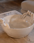 Off white ceramic bowl with twisted handles on wooden table.