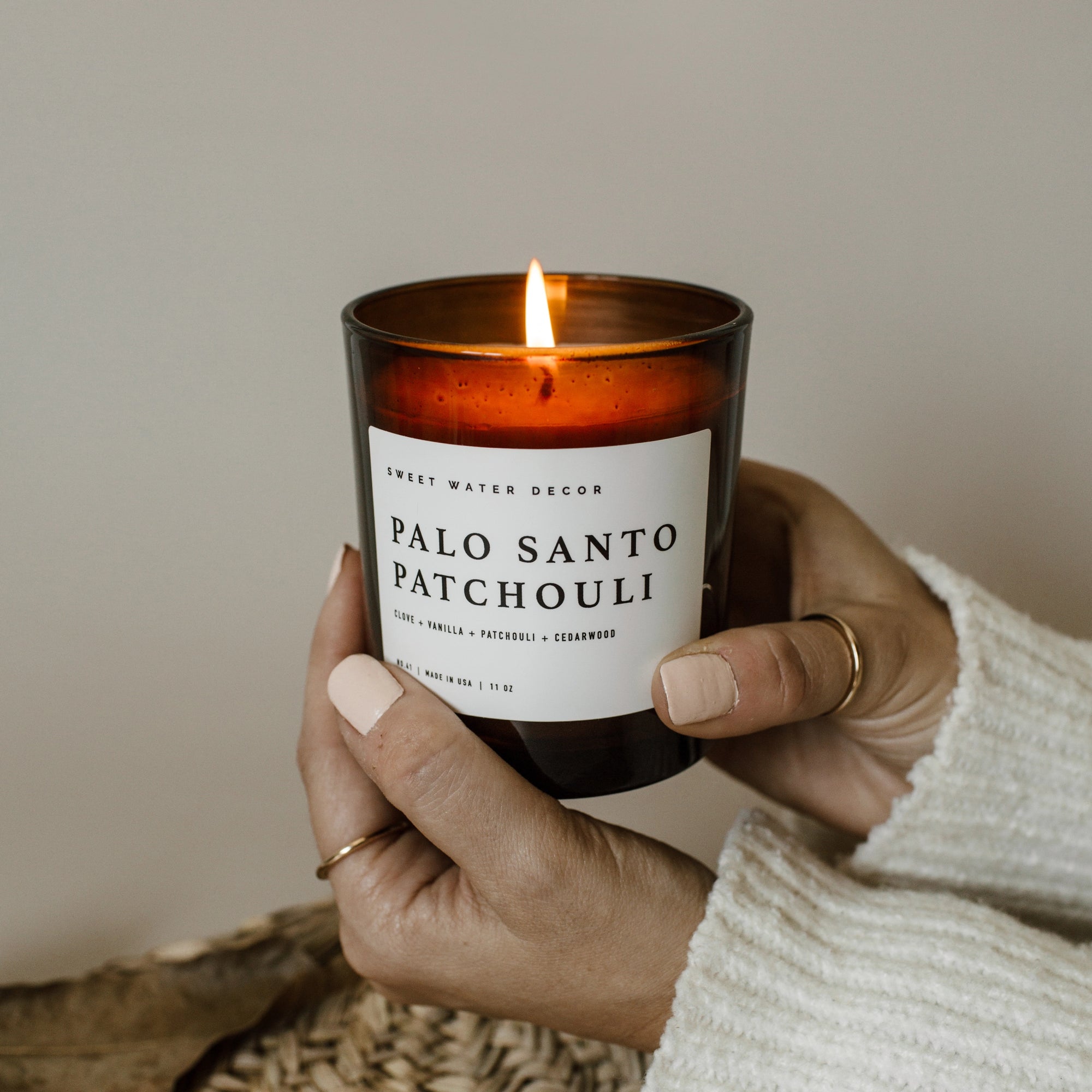 Palo santo patchouli soy candle in amber jar, lit and held up in two hands.