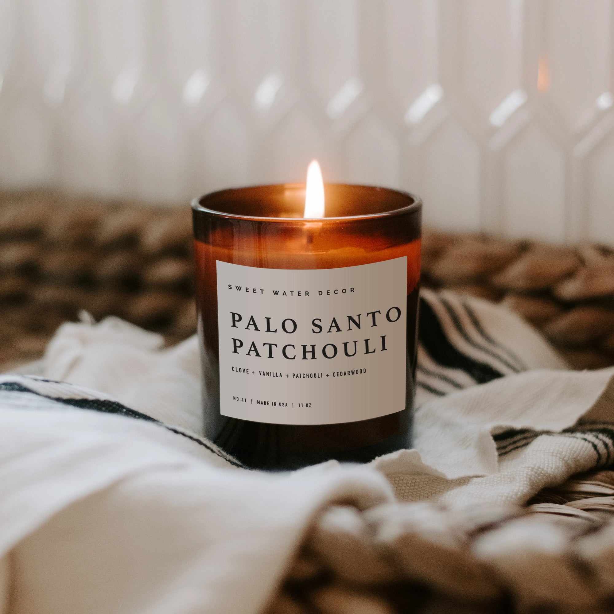 Palo santo patchouli soy candle in amber jar, lit on a towel and woven console.