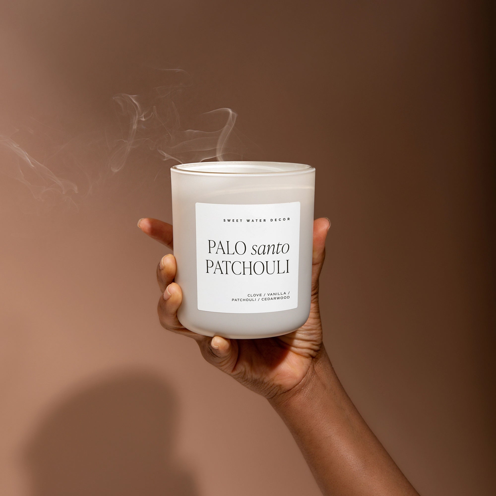 Palo Santo Patchouli soy candle in white matte jar, blown out and held up in one hand.