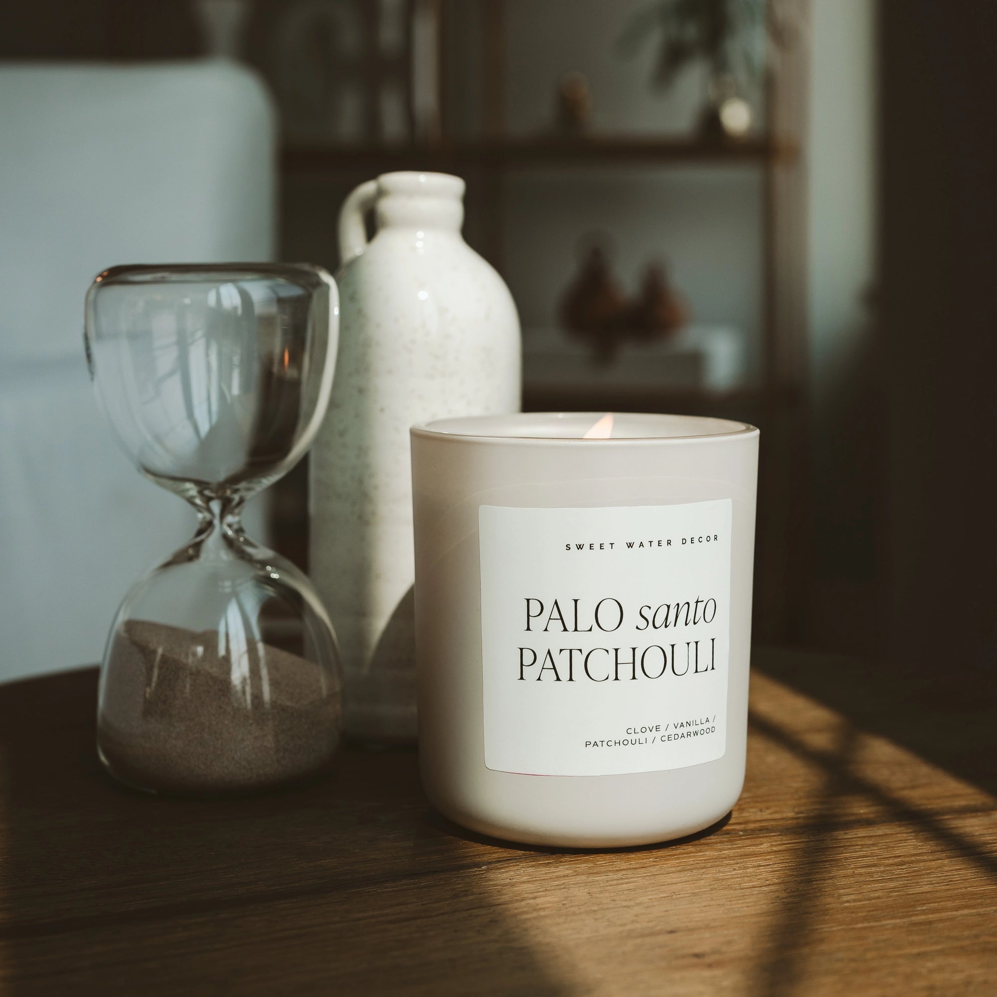 Palo Santo Patchouli soy candle in matte white jar, lit on a cupboard with other ornaments.