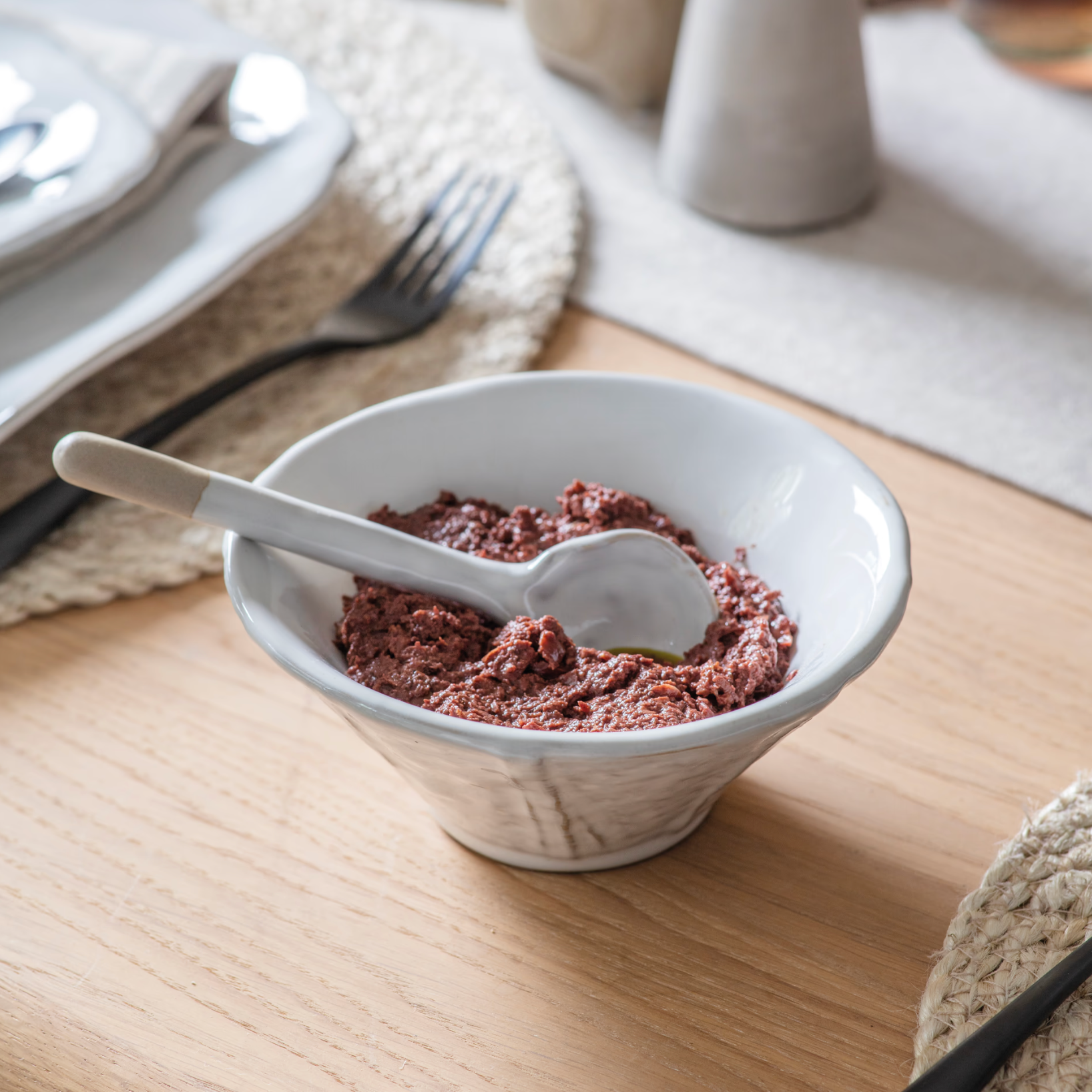 Patrycja Serving Bowl with Spoon on wooden table with tomato sauce.