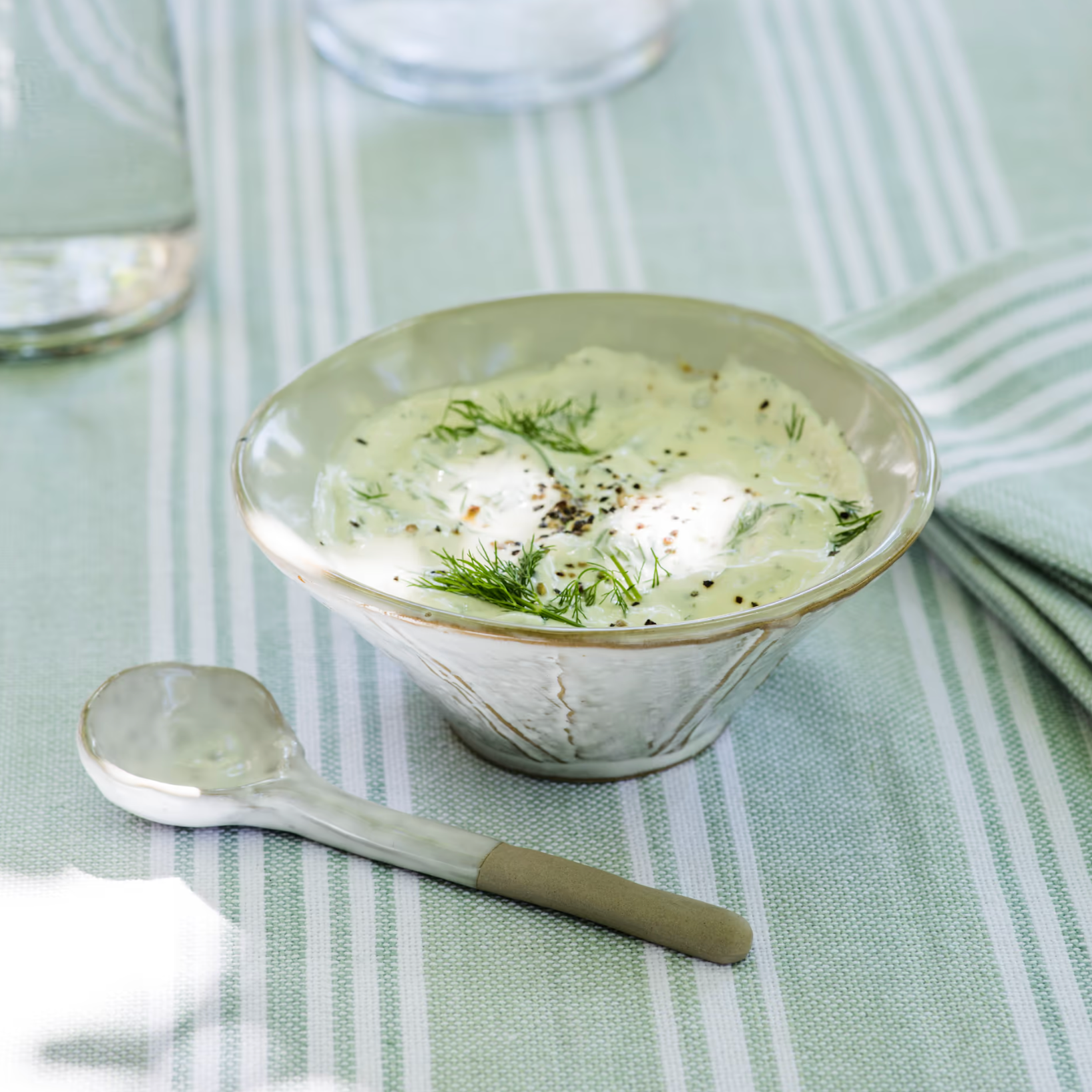 Patrycja Serving Bowl with Spoon filled with tzatziki on green table cloth.