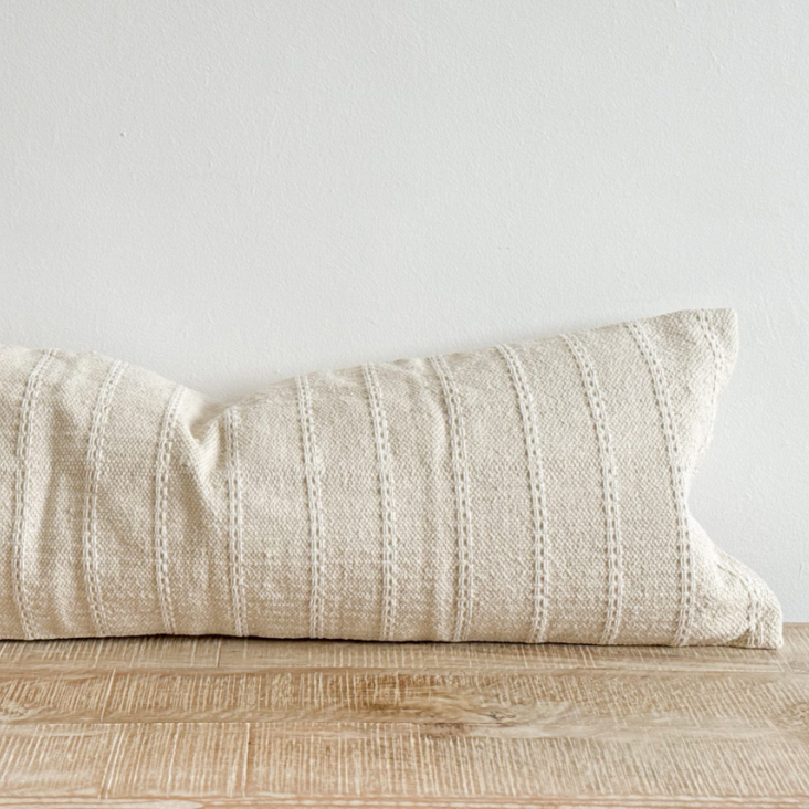 Close up of cream bolster cushion with embroidered stripes on wooden surface.