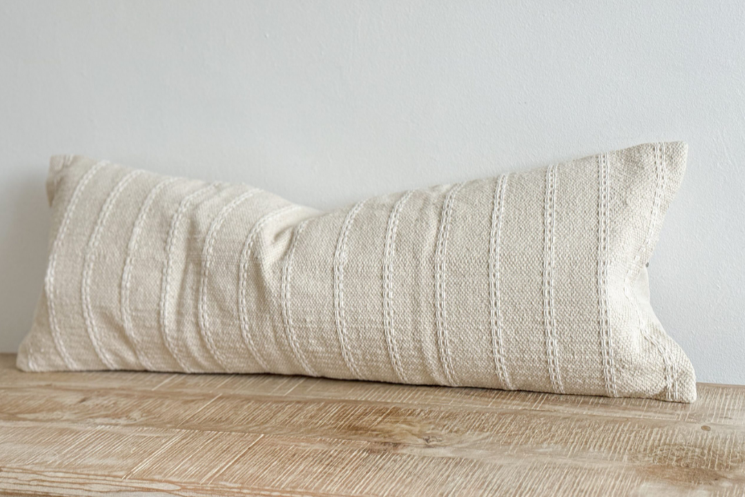 Cream bolster cushion with embroidered stripes on wooden surface.