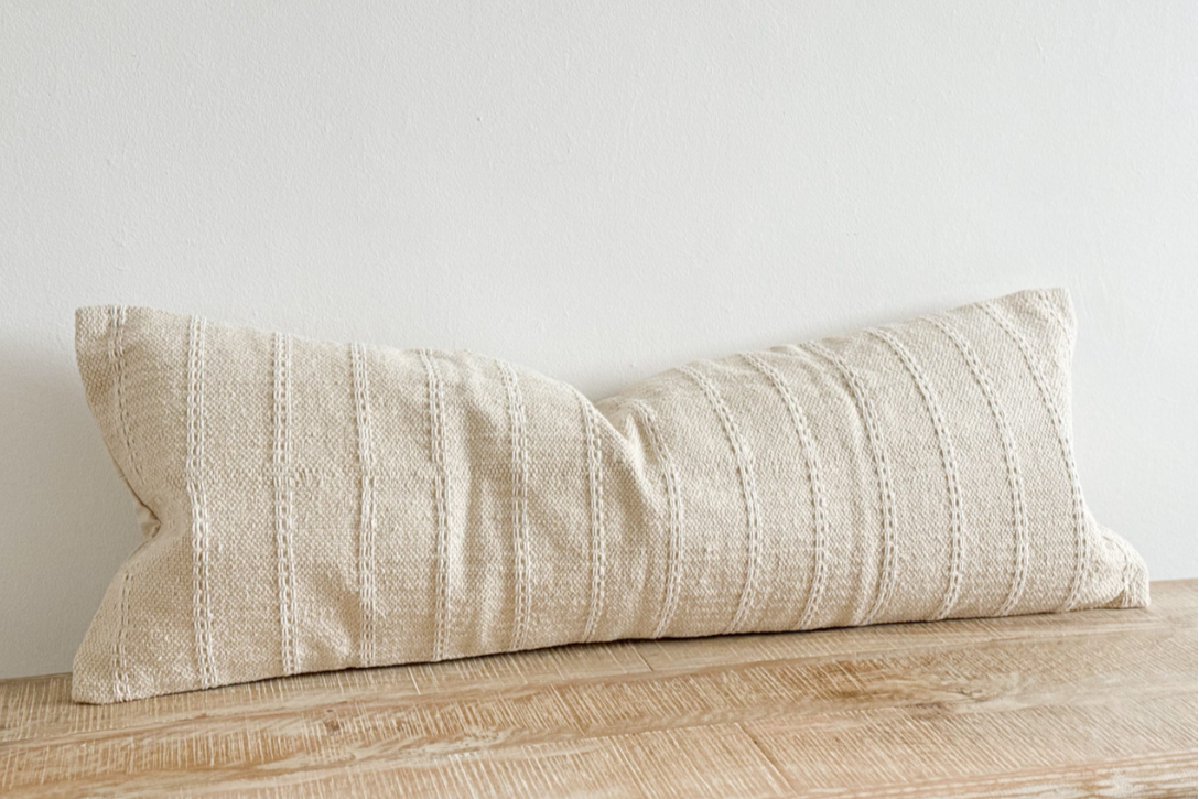 Cream bolster cushion with embroidered stripes on wooden surface.