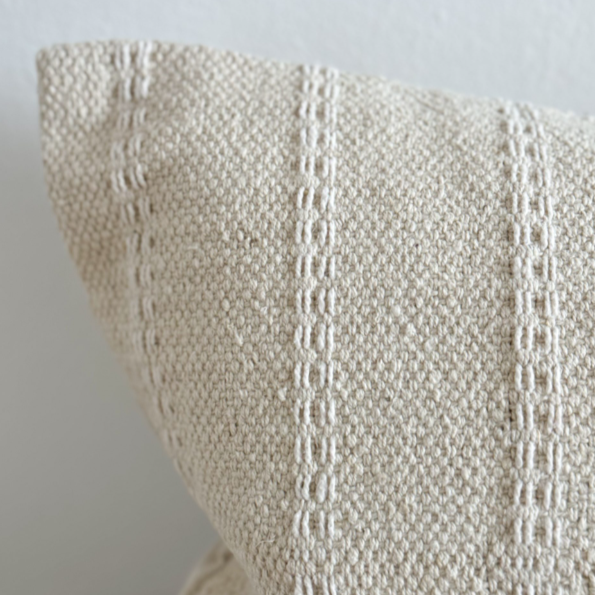 Close up of corner on cream bolster cushion with embroidered stripes.