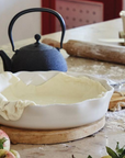 White pie dish with dough inside on floury table.
