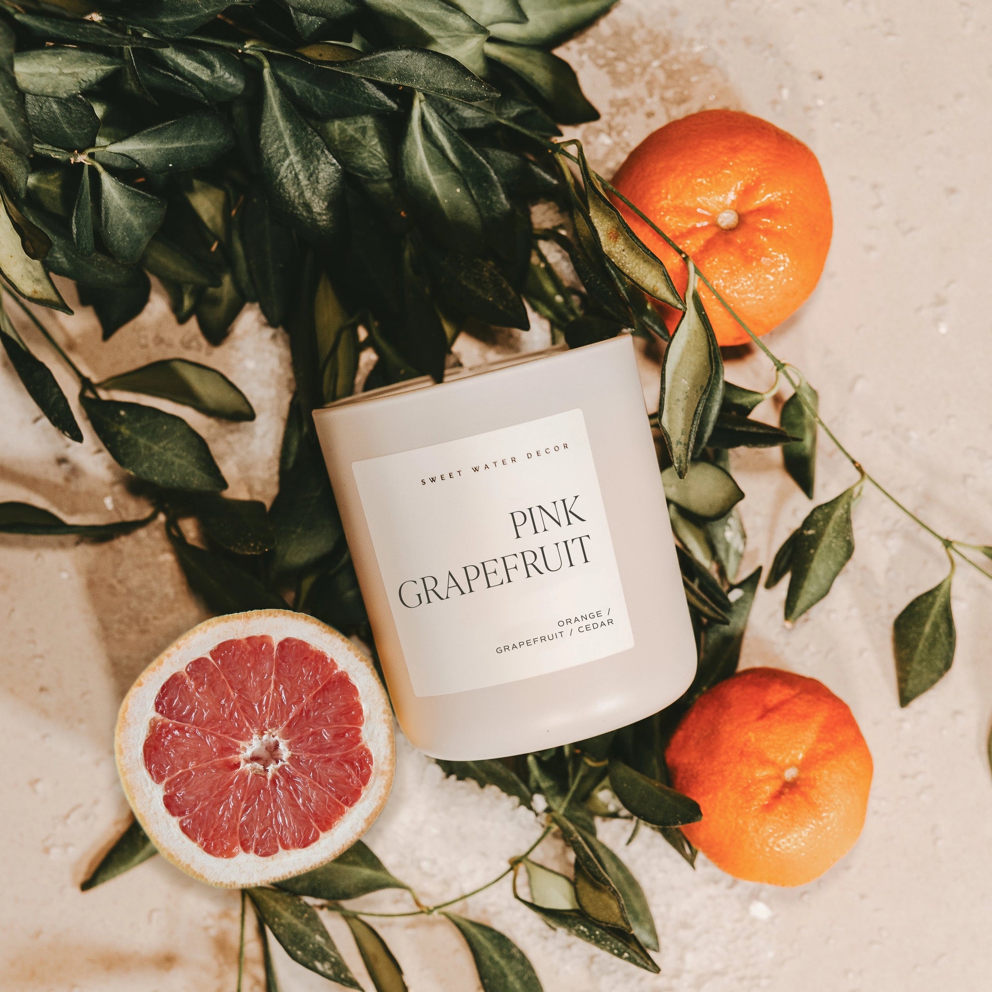 Pink grapefruit soy candle in matte white jar, with leaves and grapefruits.