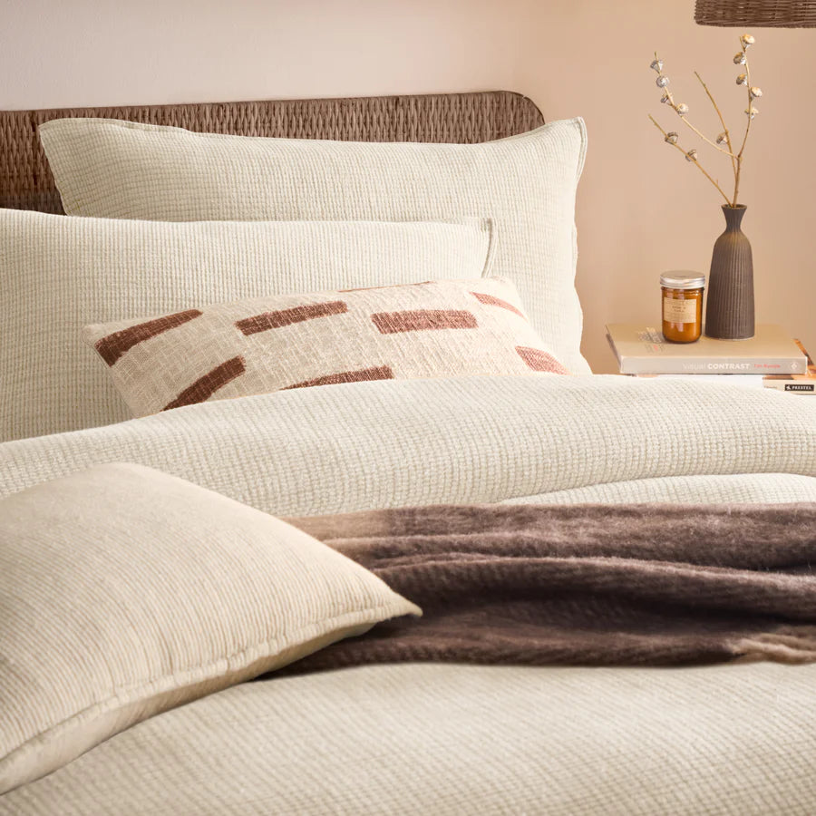 Close up of natural cream bedding set in neutral bedroom with brown accessories.