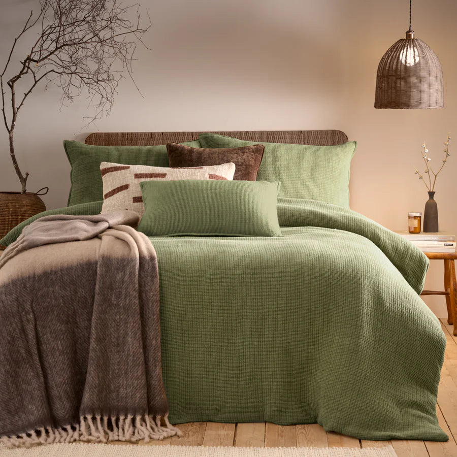 Sage green bedding set with brown and cream blankets and throws, and rattan accessories.