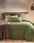 Sage green bedding set with brown and cream blankets and throws, and rattan accessories.