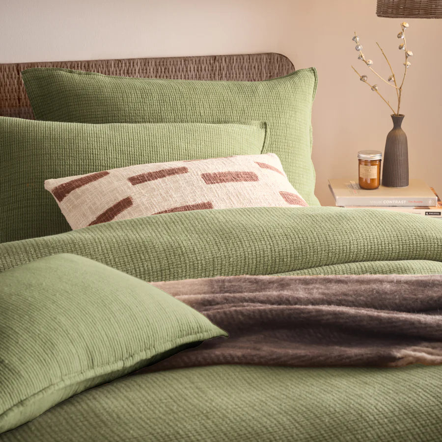 Sage green bedding sets on bed with brown throw and cream and rust patterned cushion.