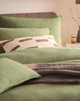 Sage green bedding sets on bed with brown throw and cream and rust patterned cushion.