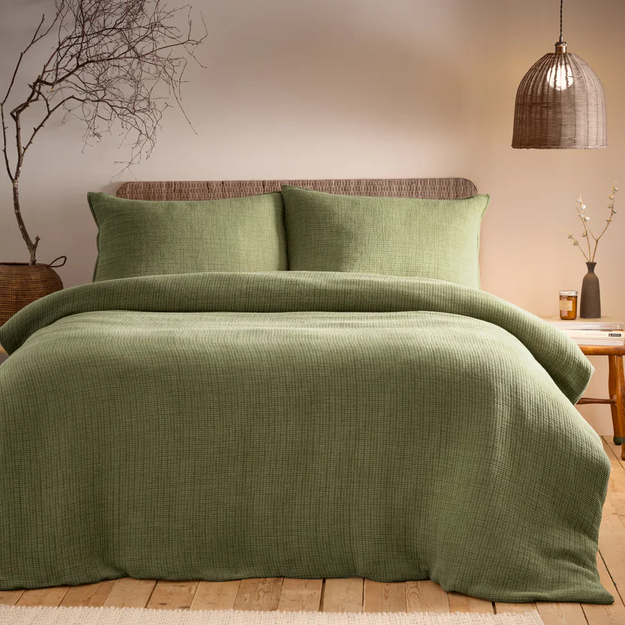 Sage green bedding set on bed with side table and rattan accessories.