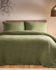 Sage green bedding set on bed with side table and rattan accessories.