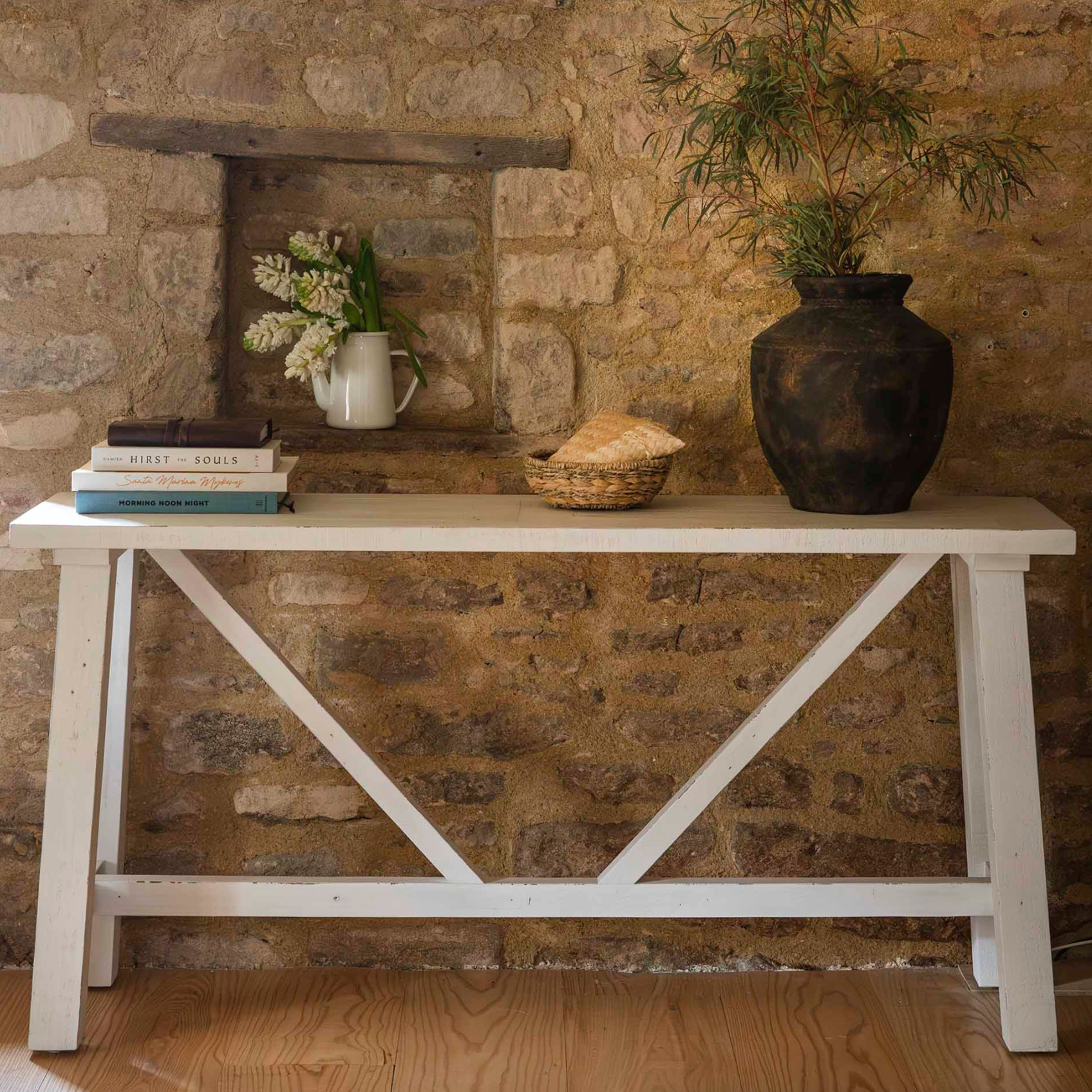 White wooden console table against exposed stone wall with plants and books.