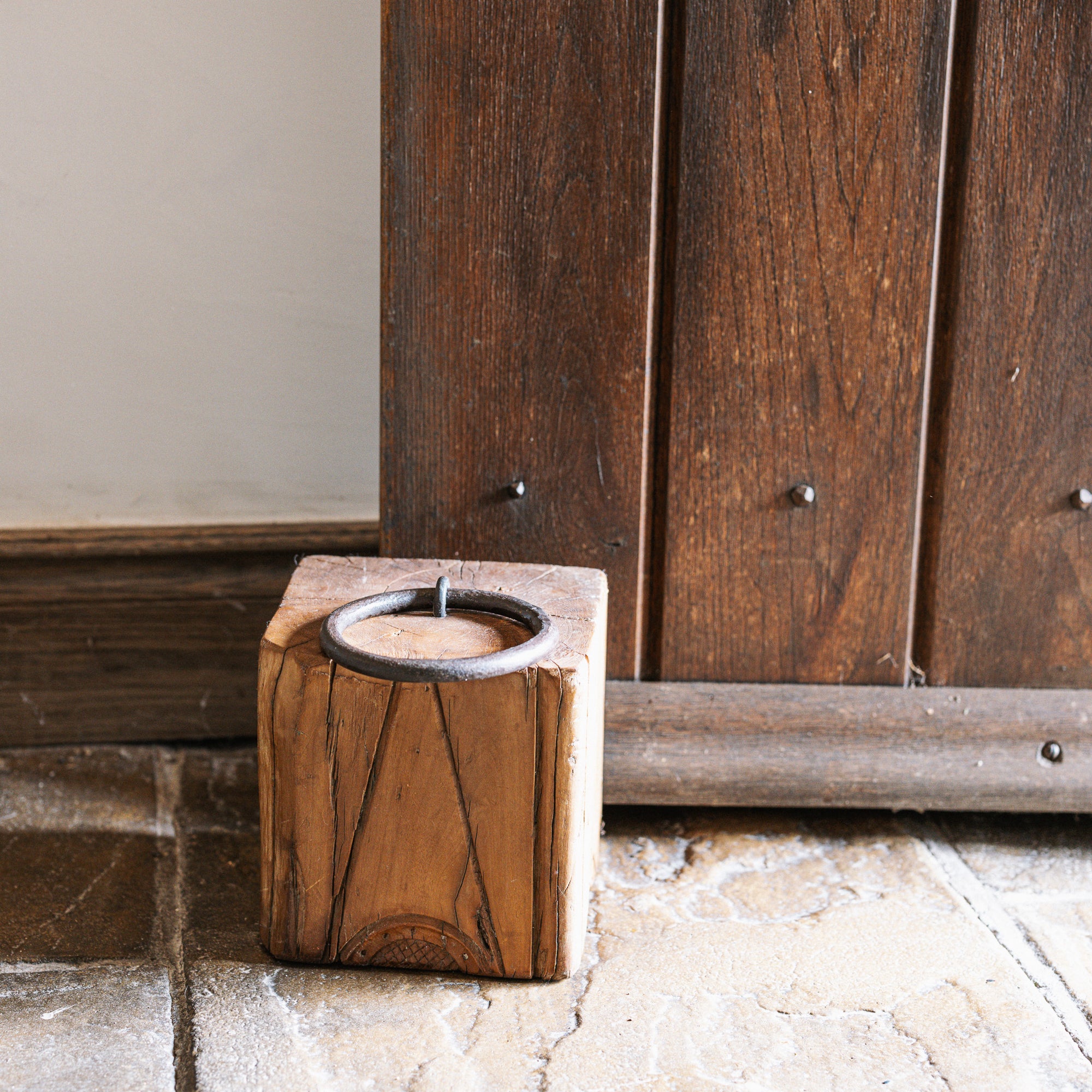 Reclaimed wooden doorstop with handle against a wooden door.