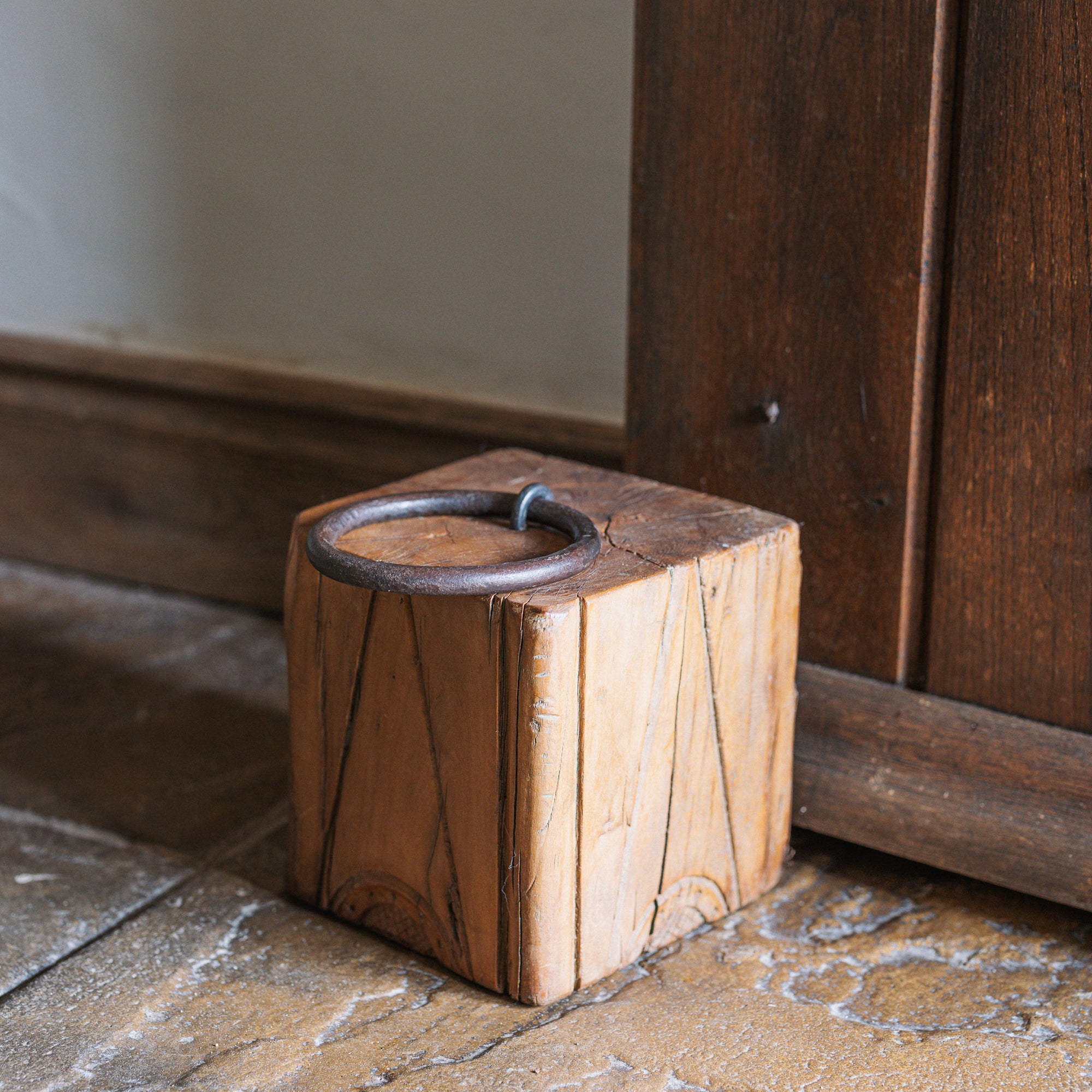 Reclaimed wooden doorstop with handle against a wooden door.