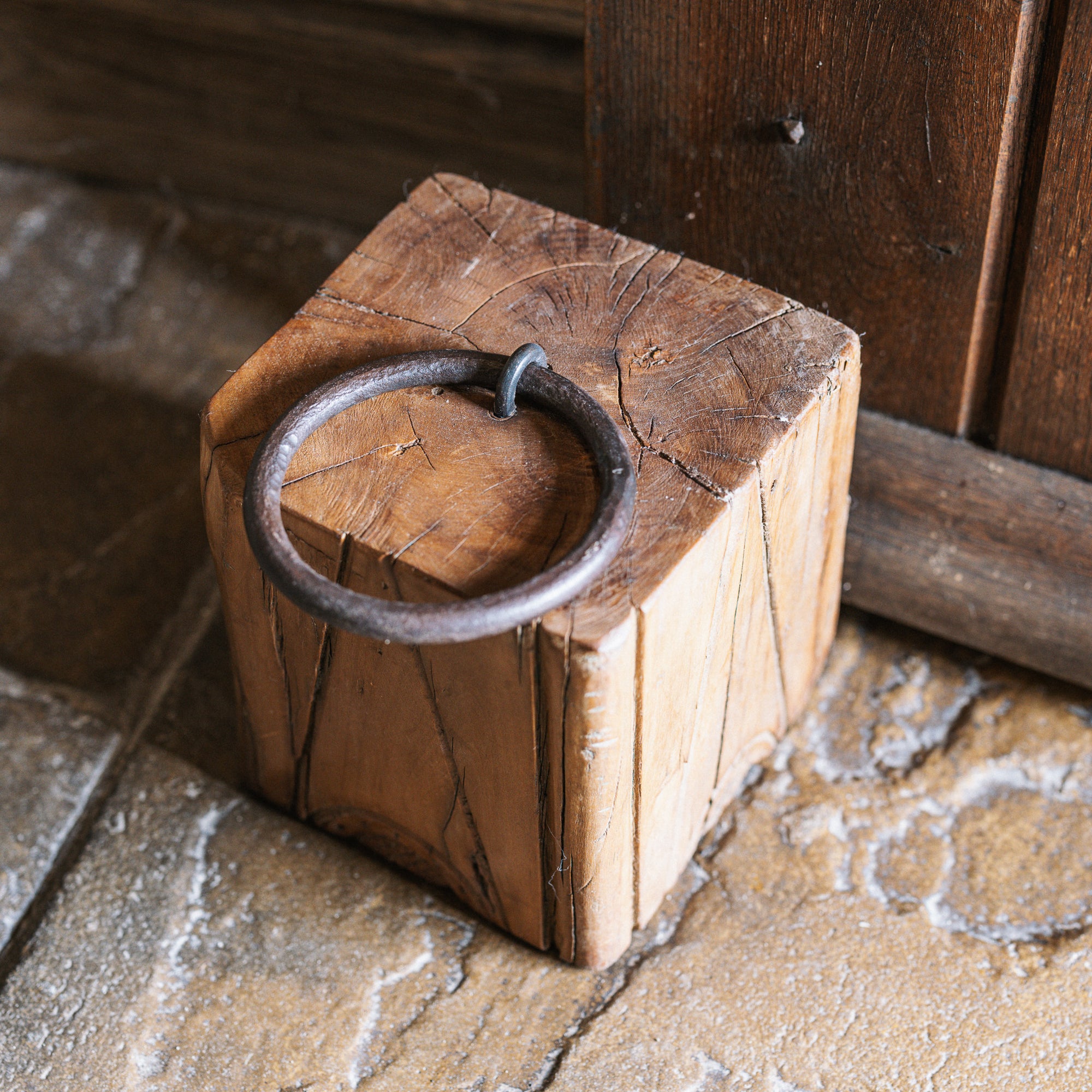 Reclaimed wooden doorstop with handle against a wooden door.