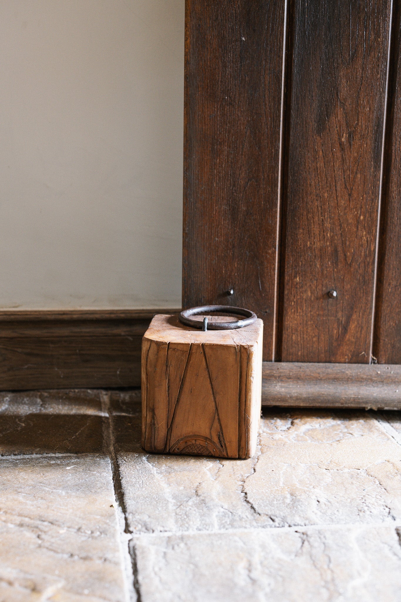 Reclaimed wooden doorstop with handle against a wooden door.