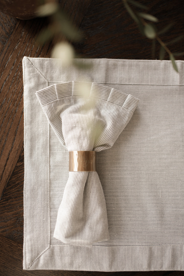 Pinstripe napkin in a brass napkin ring, on matching placemat.