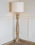 Tall wooden floor lamp switched on in the corner of a room.