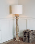 Tall wooden floor lamp switched on in the corner of a room, with a woven basket table.