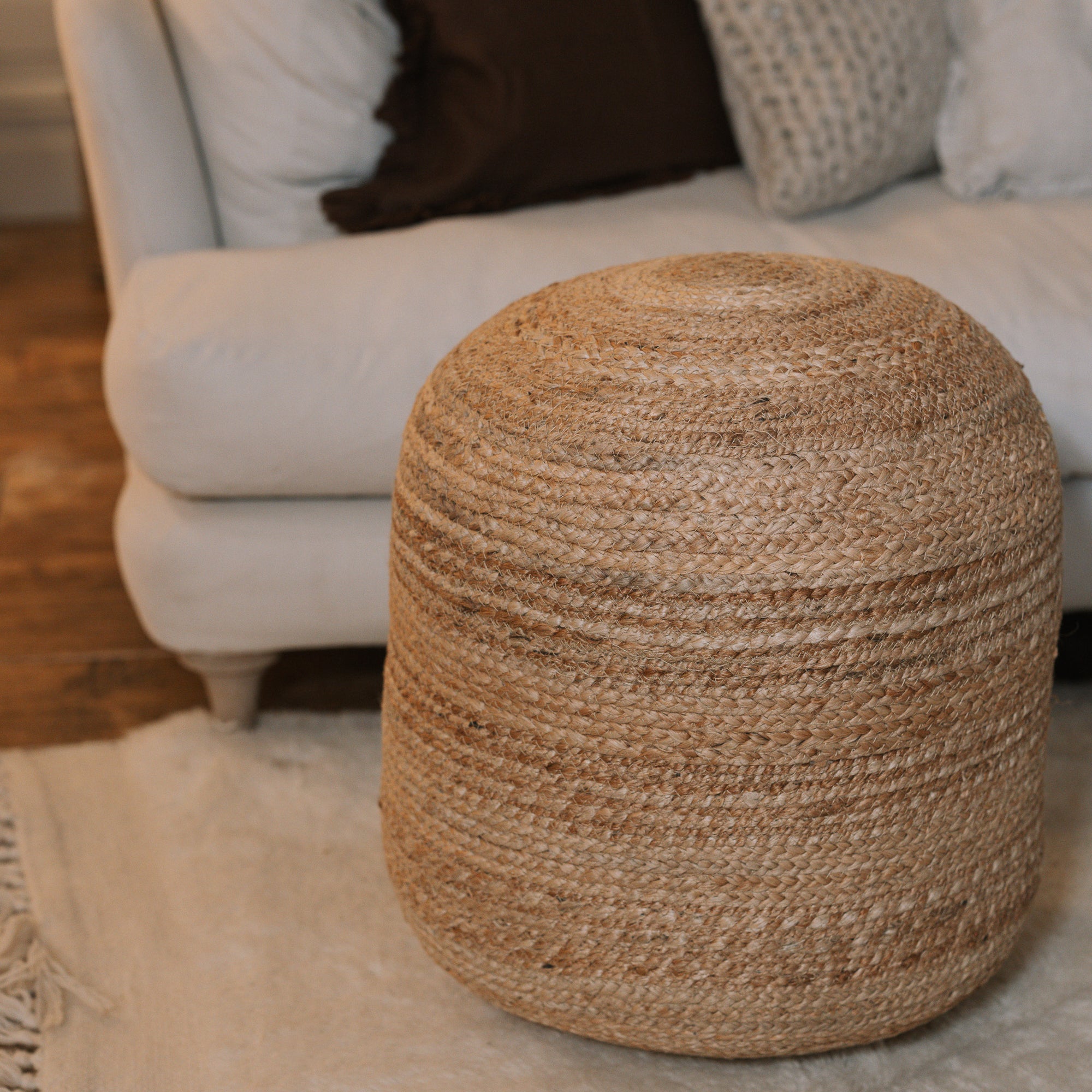 Round jute pouf in front of sofa on white rug.