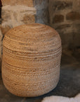 Round jute pouf by stone fire.