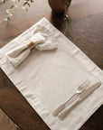 Pinstripe napkin in a brass napkin ring, on matching placemat with cutlery on dark wood dining table.