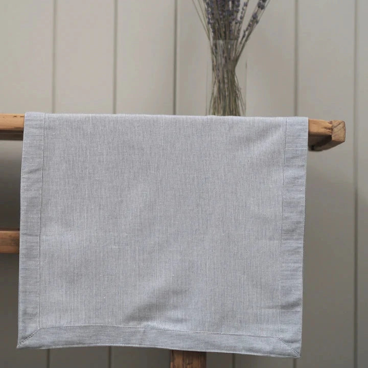 White and charcoal pinstripe table runner laid over a wooden console table with lavender in a vase. 