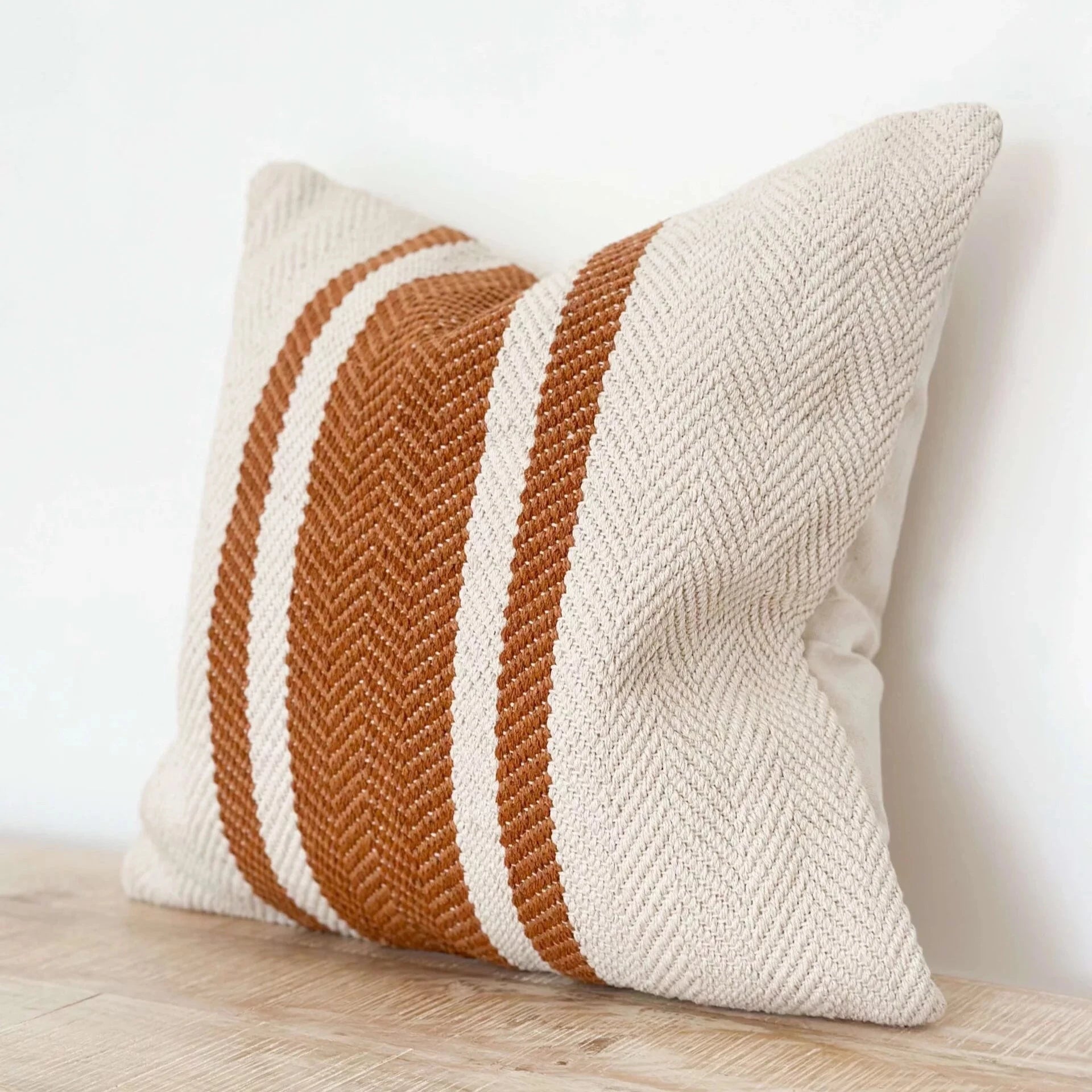 Rust and cream striped cushion on wooden surface.