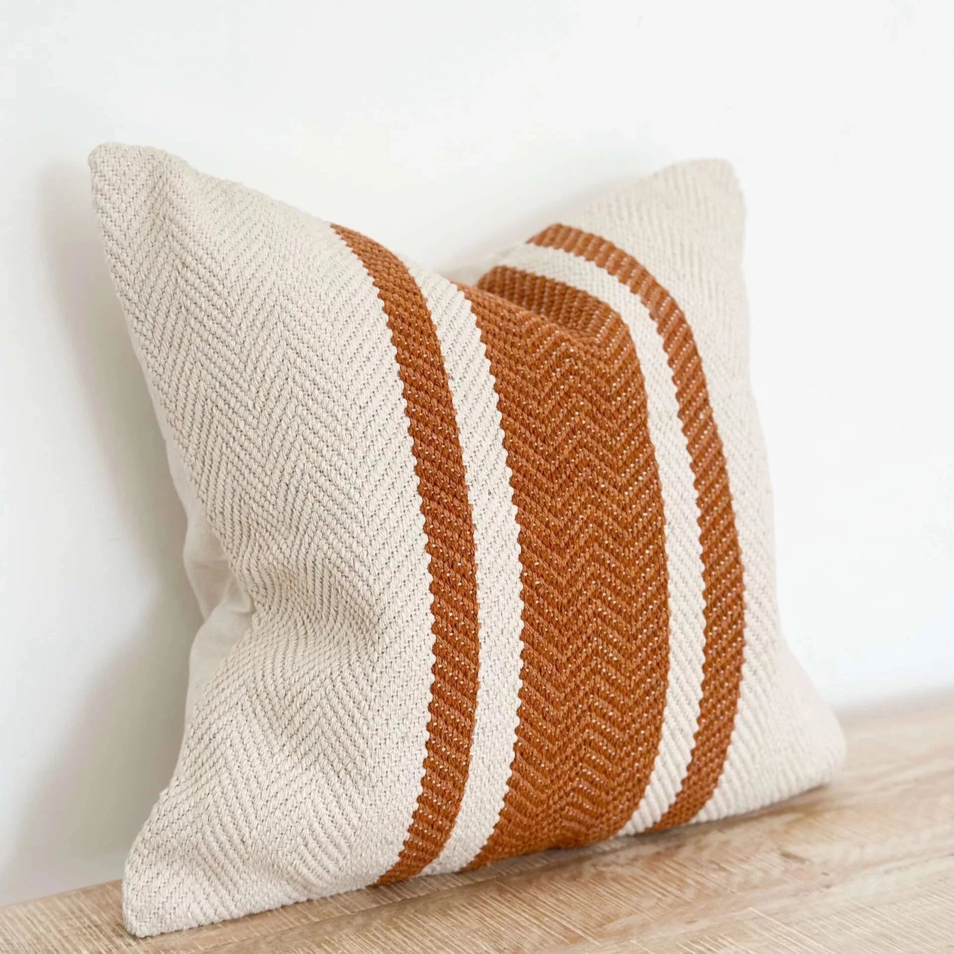 Rust and cream striped cushion on wooden surface.