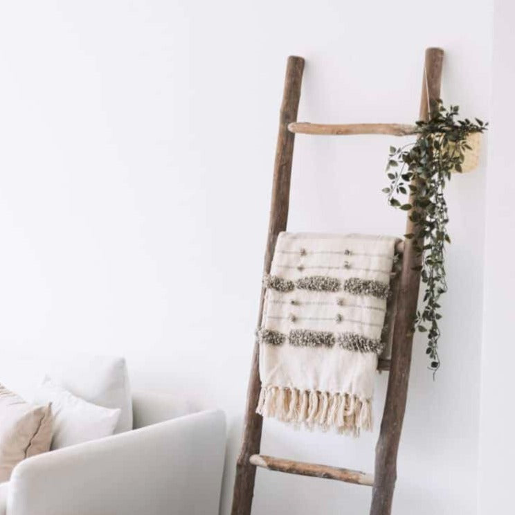 Wooden ladder with white tassled blanket hanging over and greenery.