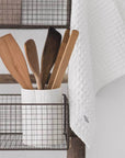 Close up of wire baskets on wooden storage ladder with kitchen utensils in white pot.