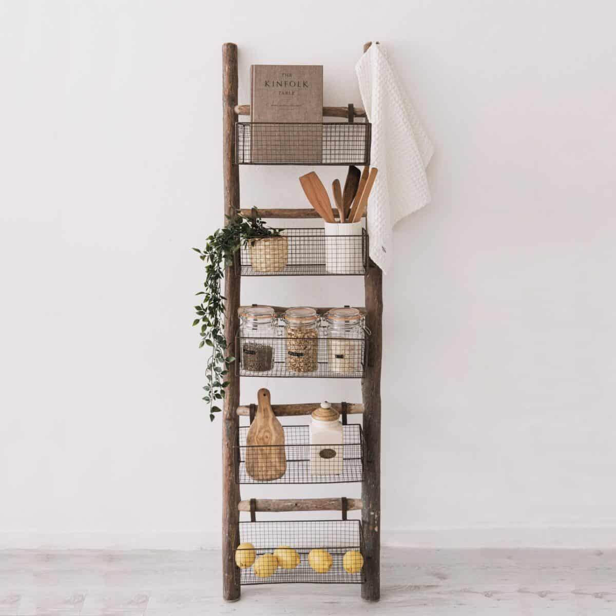 Storage ladder with baskets filled with kitchen utensils, fruit, and greenery.
