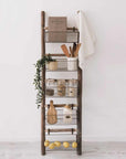 Storage ladder with baskets filled with kitchen utensils, fruit, and greenery.